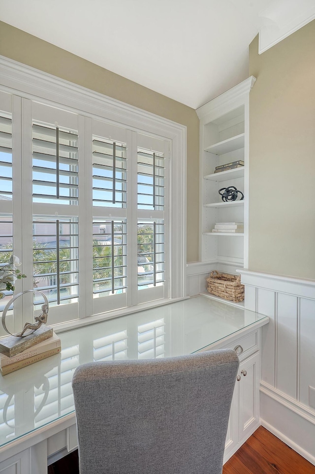 office space featuring built in features, dark wood-style flooring, a wainscoted wall, and a decorative wall