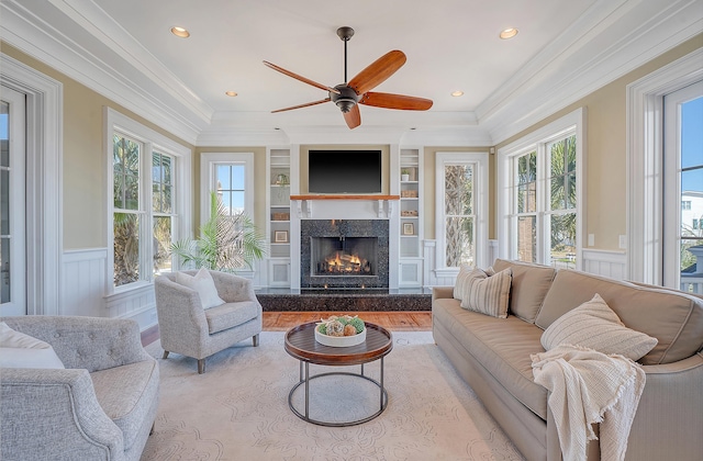 living area featuring built in features, a fireplace, crown molding, recessed lighting, and wainscoting