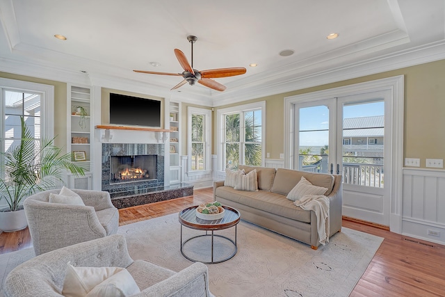 living room with built in shelves, wainscoting, a raised ceiling, and a healthy amount of sunlight