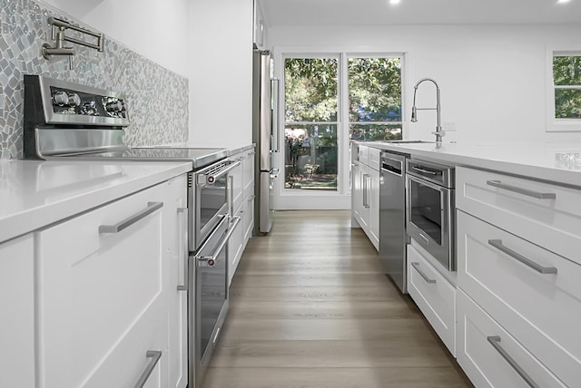 kitchen with light hardwood / wood-style flooring, sink, backsplash, appliances with stainless steel finishes, and white cabinetry