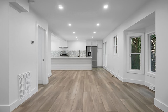 kitchen with white cabinetry, range, stainless steel fridge with ice dispenser, light hardwood / wood-style floors, and decorative backsplash