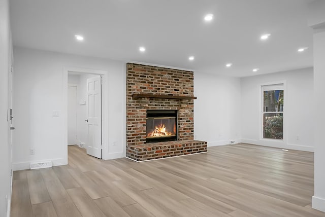 unfurnished living room featuring a brick fireplace and light wood-type flooring