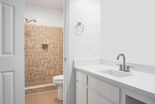 bathroom featuring toilet, a tile shower, and vanity