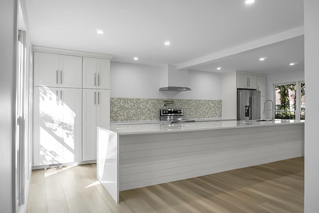 kitchen with white cabinetry, appliances with stainless steel finishes, wall chimney range hood, and light wood-type flooring