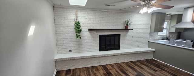 unfurnished living room featuring brick wall, dark hardwood / wood-style floors, sink, ceiling fan, and a brick fireplace