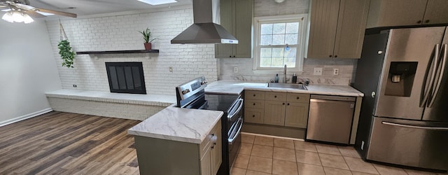 kitchen featuring sink, a skylight, a brick fireplace, stainless steel appliances, and wall chimney range hood