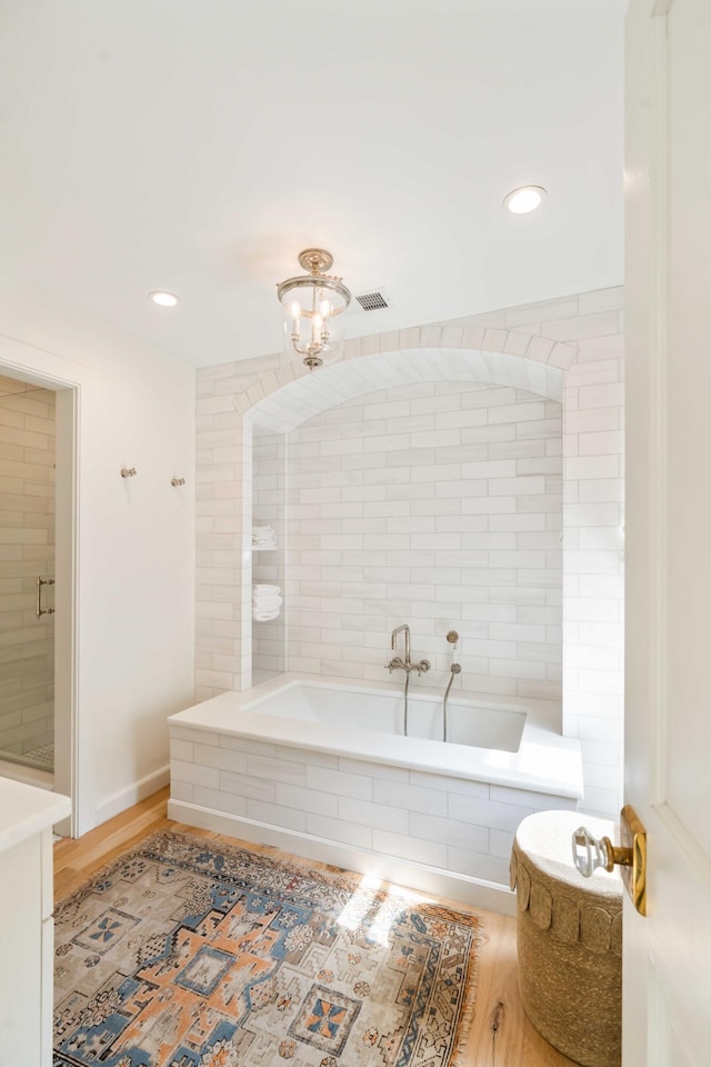 bathroom with visible vents, recessed lighting, a bath, and wood finished floors