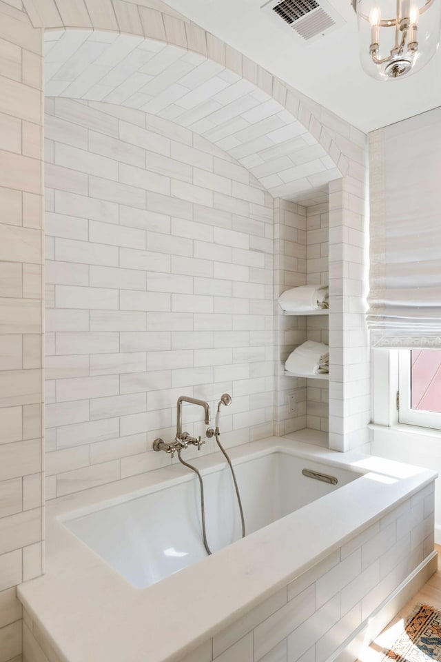 bathroom featuring a garden tub, a chandelier, and visible vents