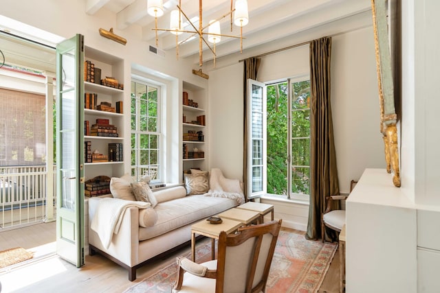 sitting room with a chandelier, built in shelves, light wood-style flooring, beamed ceiling, and visible vents