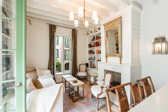 sitting room with a notable chandelier, beam ceiling, a fireplace, built in features, and wood finished floors