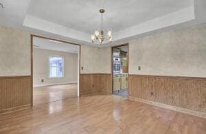 unfurnished room with a raised ceiling, wooden walls, wood-type flooring, and an inviting chandelier