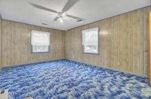 empty room featuring wood walls, carpet floors, and ceiling fan