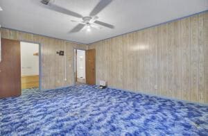 carpeted spare room featuring ceiling fan and wood walls