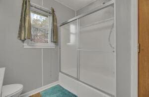 bathroom with toilet and bath / shower combo with glass door