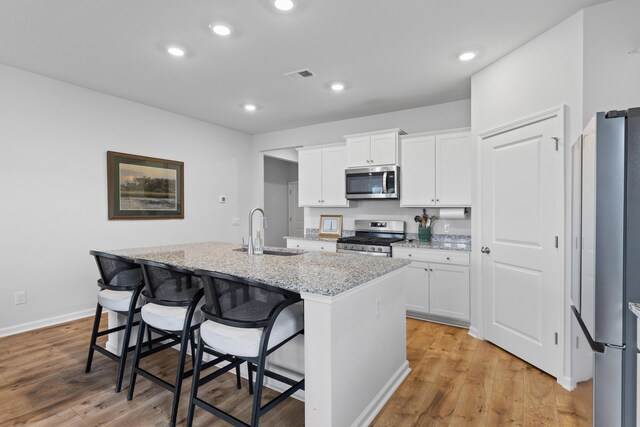 1173 Wading Point Blvd, Huger, SC 29450 - kitchen featuring appliances with stainless steel finishes, a sink, a kitchen island with sink, white cabinets, and light stone counters