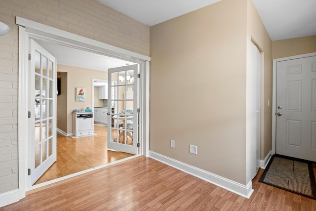 interior space featuring a chandelier, french doors, light hardwood / wood-style flooring, and brick wall