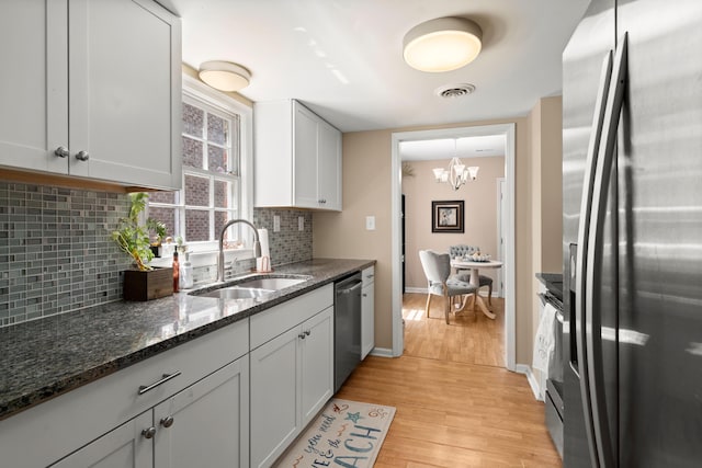 kitchen featuring dark stone counters, sink, light hardwood / wood-style flooring, decorative backsplash, and stainless steel appliances