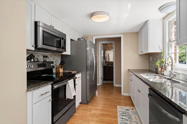 kitchen with appliances with stainless steel finishes, dark stone counters, sink, light hardwood / wood-style flooring, and white cabinetry