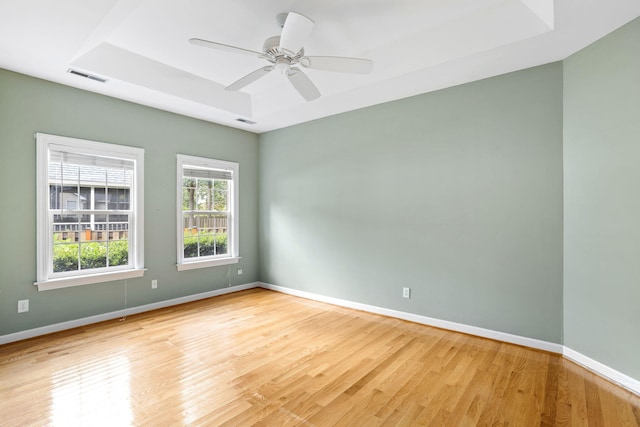 empty room featuring light wood-type flooring, a tray ceiling, and ceiling fan