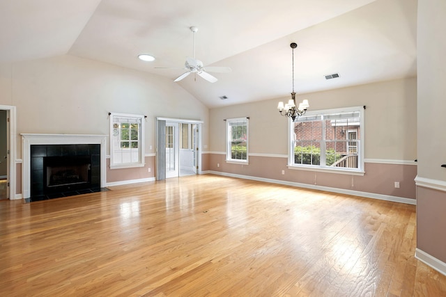 unfurnished living room with vaulted ceiling, light wood-type flooring, ceiling fan with notable chandelier, and a tile fireplace