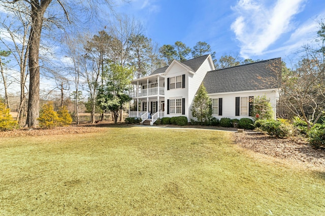 colonial-style house with a front yard, covered porch, roof with shingles, and a balcony