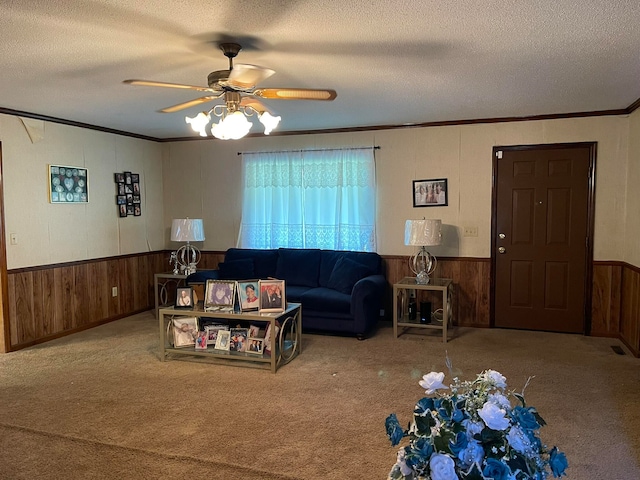 carpeted living room featuring ceiling fan, a textured ceiling, wood walls, and ornamental molding