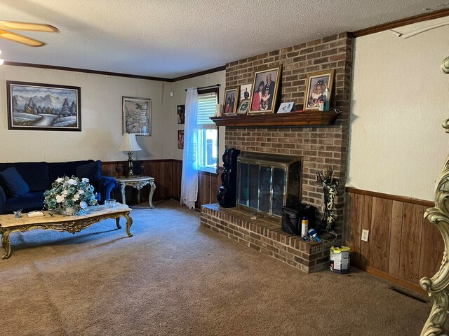 living room with a brick fireplace, ceiling fan, crown molding, carpet, and a textured ceiling