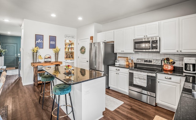 kitchen featuring a kitchen breakfast bar, dark wood finished floors, appliances with stainless steel finishes, white cabinets, and decorative backsplash