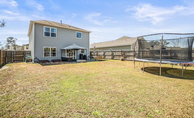 back of property featuring a yard, a trampoline, a fenced backyard, and a patio area