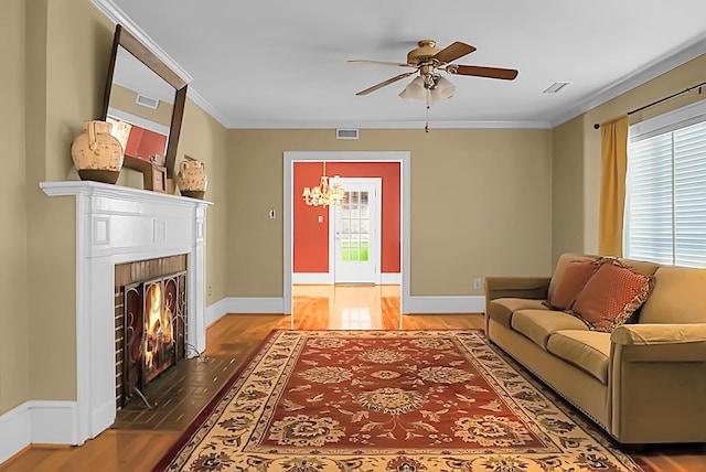 living room with ceiling fan with notable chandelier, ornamental molding, a fireplace, and wood-type flooring