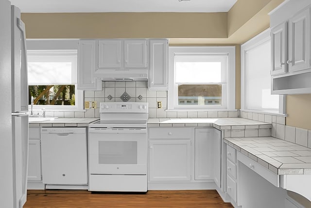 kitchen with tile countertops, backsplash, white appliances, light wood-type flooring, and white cabinets