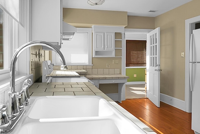 kitchen with tile counters, wood-type flooring, white refrigerator, and white cabinetry