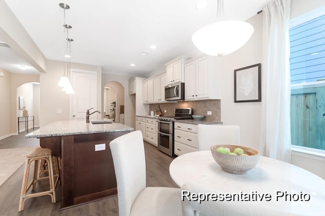 kitchen with appliances with stainless steel finishes, arched walkways, white cabinets, and a sink