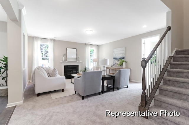 carpeted living room featuring a healthy amount of sunlight, stairs, baseboards, and a glass covered fireplace