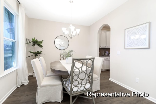 dining room featuring dark wood-style floors, a notable chandelier, arched walkways, and baseboards