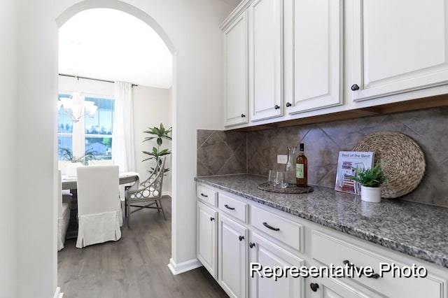 kitchen with arched walkways, light stone countertops, dark wood-style flooring, white cabinets, and decorative backsplash