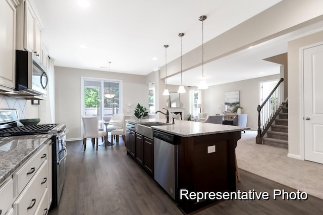 kitchen with appliances with stainless steel finishes, open floor plan, a sink, and light stone counters