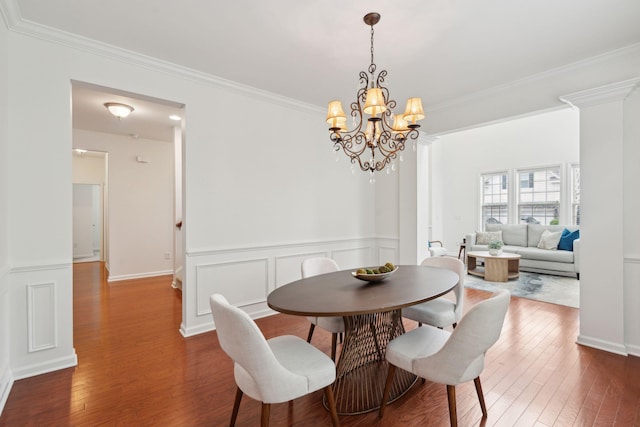dining room with a chandelier, hardwood / wood-style floors, crown molding, wainscoting, and a decorative wall