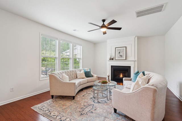 living room featuring baseboards, ceiling fan, a fireplace, and dark wood-style flooring