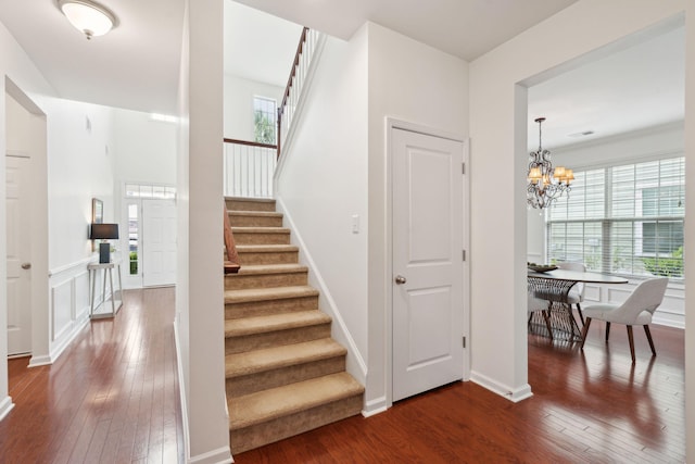stairs featuring hardwood / wood-style floors, healthy amount of natural light, and a chandelier