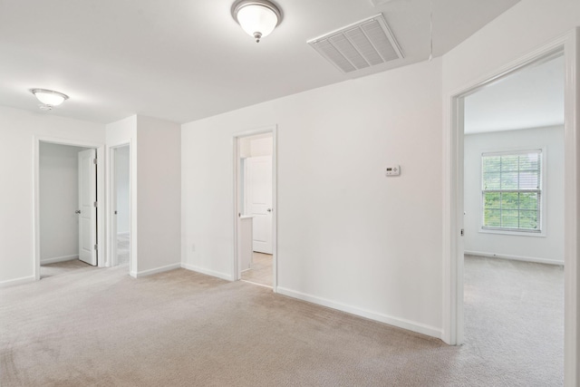 unfurnished bedroom featuring light colored carpet, baseboards, attic access, and ensuite bath