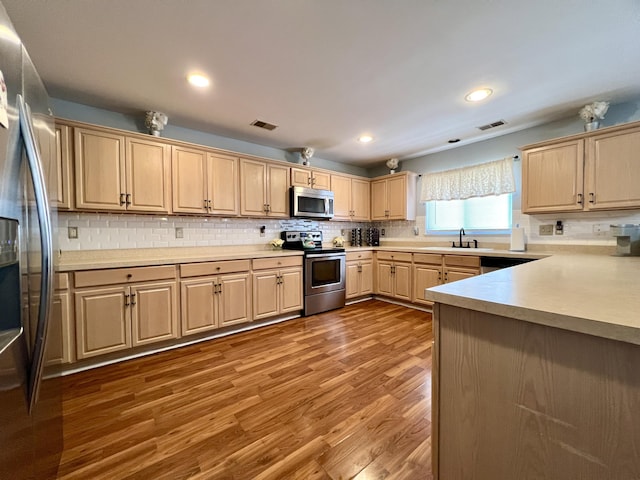 kitchen featuring appliances with stainless steel finishes, backsplash, sink, light brown cabinets, and wood-type flooring