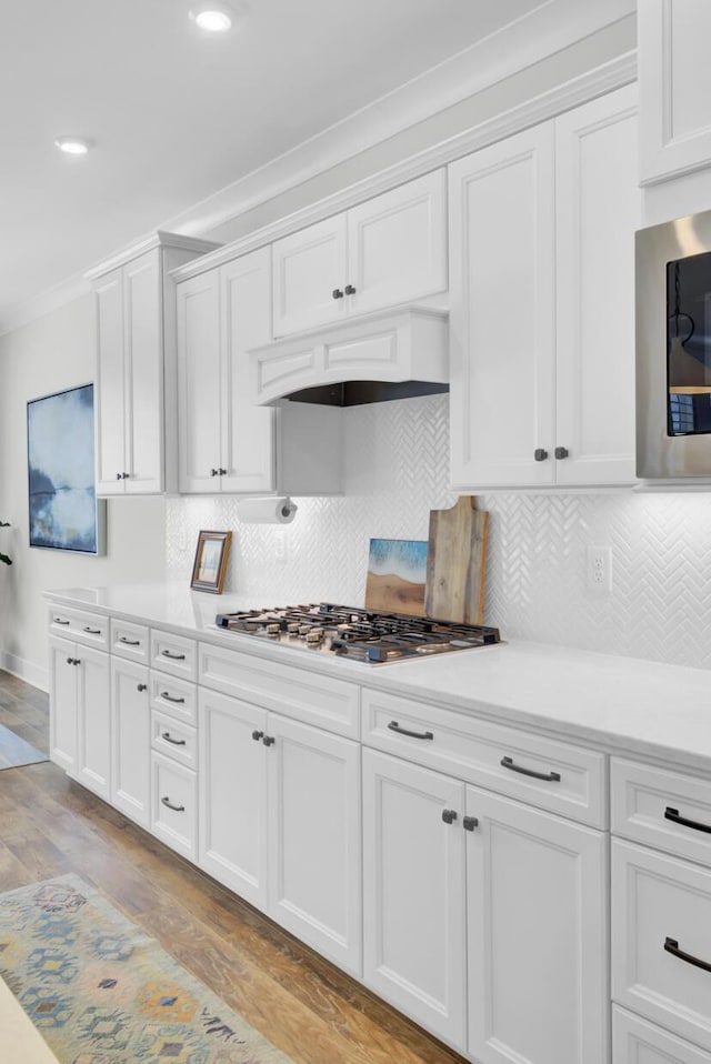kitchen featuring light wood-style flooring, stainless steel gas stovetop, custom range hood, white cabinets, and crown molding