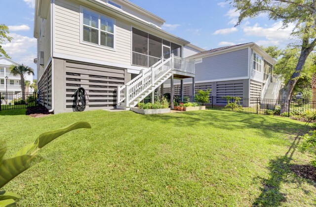 rear view of house featuring a sunroom, a lawn, stairway, and fence