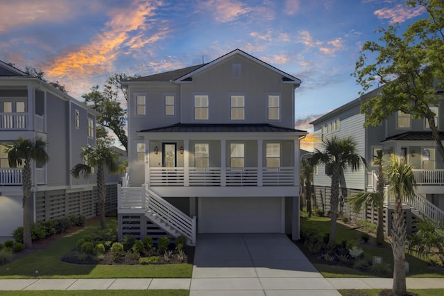 beach home featuring a porch, stairway, a standing seam roof, a garage, and driveway