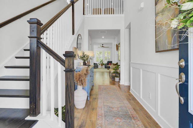 foyer entrance featuring wood-type flooring, a towering ceiling, a ceiling fan, and stairway