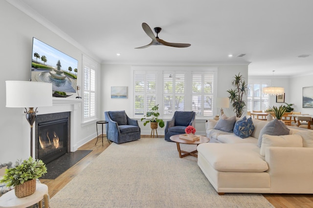 living room featuring recessed lighting, a fireplace with flush hearth, ornamental molding, wood finished floors, and ceiling fan with notable chandelier