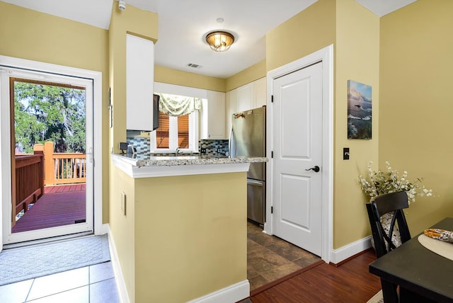 kitchen with decorative backsplash, dark wood-type flooring, kitchen peninsula, white cabinetry, and stainless steel refrigerator