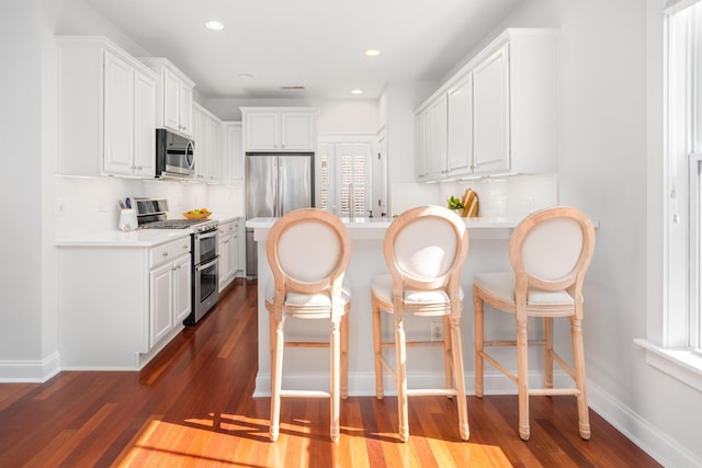 kitchen with backsplash, a breakfast bar, appliances with stainless steel finishes, a peninsula, and dark wood-style flooring