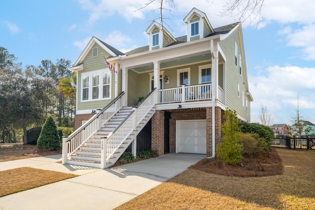 beach home with a porch, concrete driveway, a garage, brick siding, and stairs